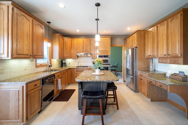 kitchen with light stone counters, a kitchen island, a sink, under cabinet range hood, and appliances with stainless steel finishes