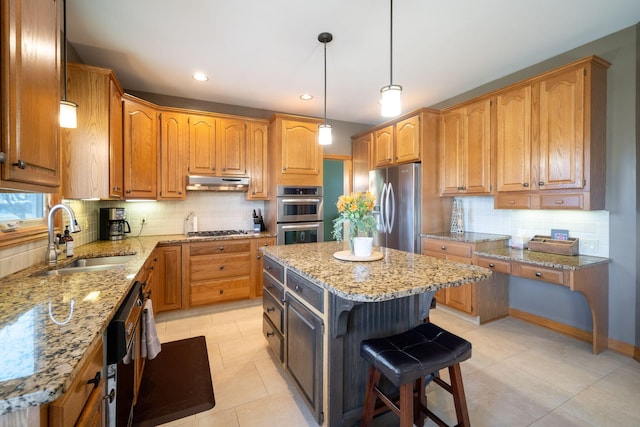 kitchen with under cabinet range hood, light stone counters, appliances with stainless steel finishes, and a sink