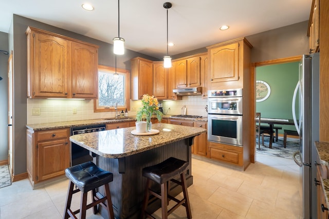 kitchen with a kitchen bar, under cabinet range hood, a sink, a center island, and appliances with stainless steel finishes