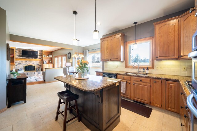 kitchen with light stone counters, a fireplace, a sink, open floor plan, and a center island