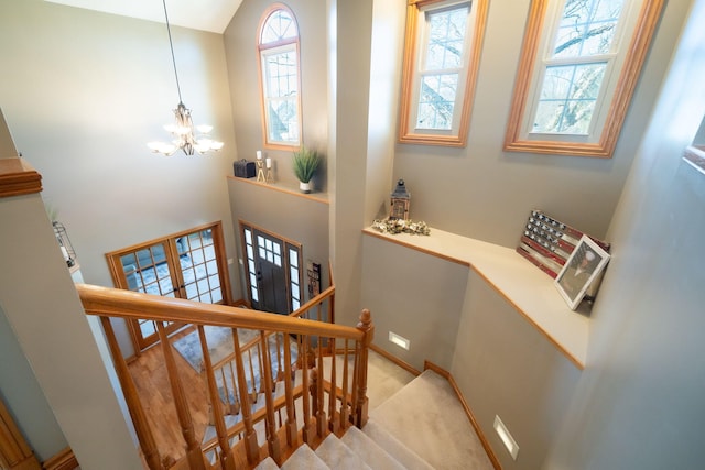 stairs with a wealth of natural light, a notable chandelier, baseboards, and carpet