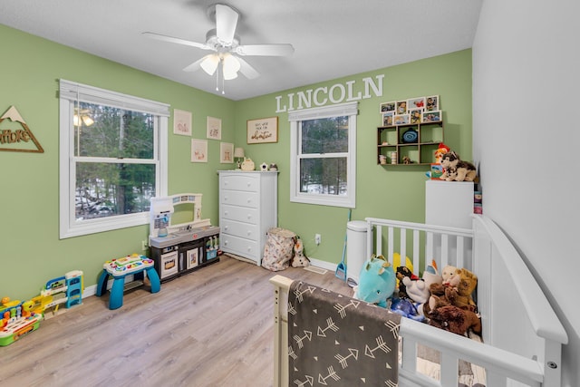 bedroom with a crib, wood finished floors, baseboards, and a ceiling fan