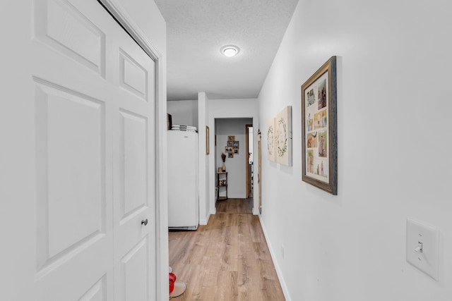 corridor featuring baseboards, light wood finished floors, and a textured ceiling