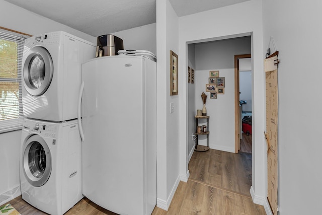 washroom featuring laundry area, light wood-style flooring, stacked washer / drying machine, and baseboards