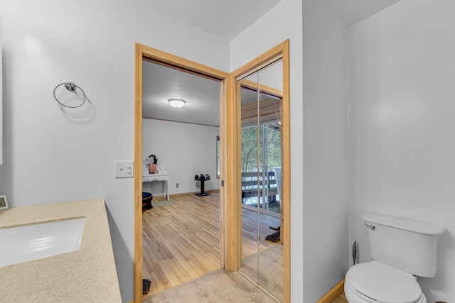 bathroom featuring toilet, wood finished floors, baseboards, and a sink