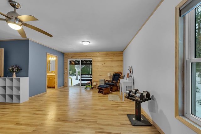 living area with wood finished floors, baseboards, ceiling fan, ornamental molding, and wood walls