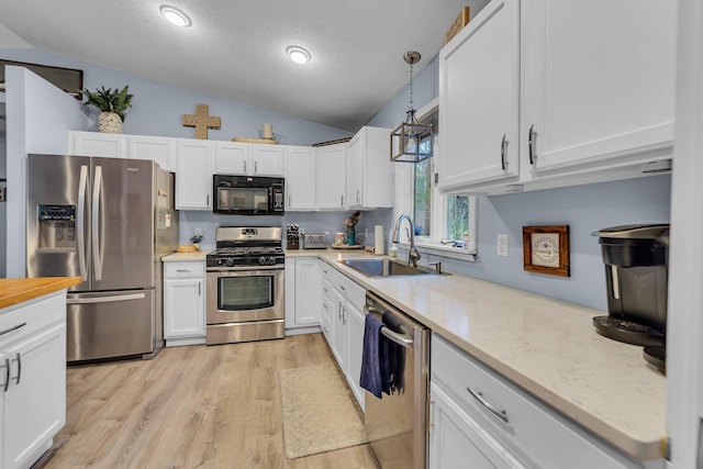 kitchen featuring light wood-style flooring, a sink, white cabinetry, stainless steel appliances, and hanging light fixtures