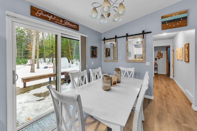 dining room featuring baseboards, lofted ceiling, a barn door, wood finished floors, and a notable chandelier