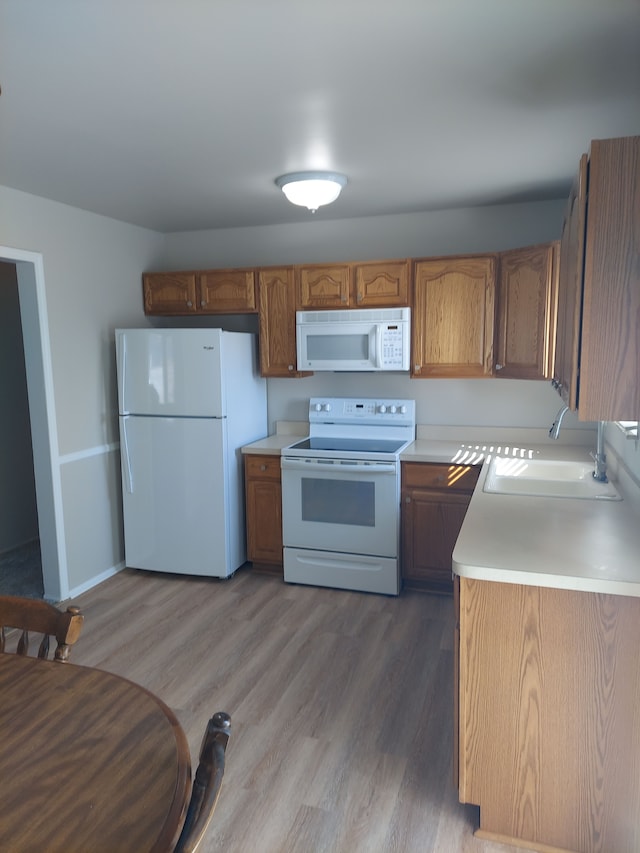 kitchen with brown cabinets, a sink, white appliances, light wood finished floors, and light countertops