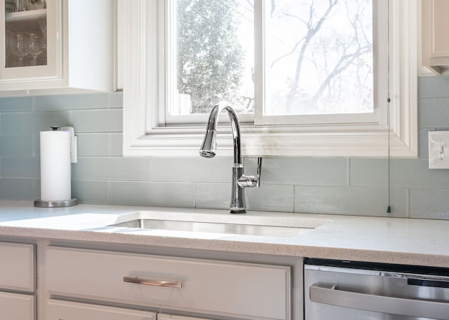 interior details with dishwasher, decorative backsplash, white cabinets, and a sink