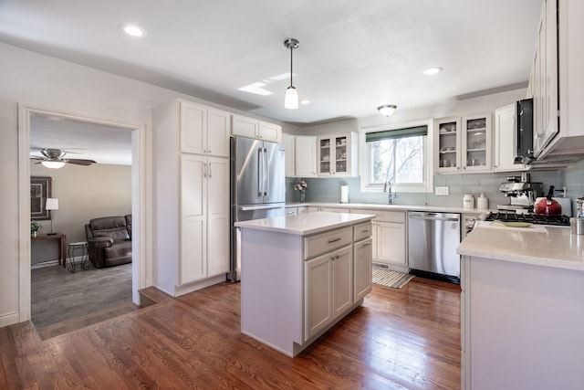 kitchen with tasteful backsplash, a kitchen island, light countertops, stainless steel appliances, and dark wood-style flooring