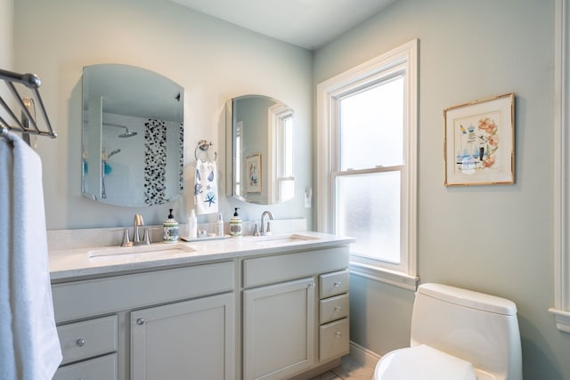 bathroom with toilet, double vanity, walk in shower, and a sink