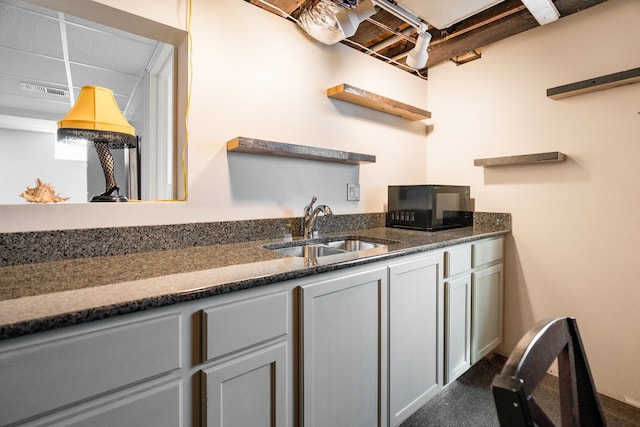 kitchen with open shelves, visible vents, dark stone countertops, and a sink