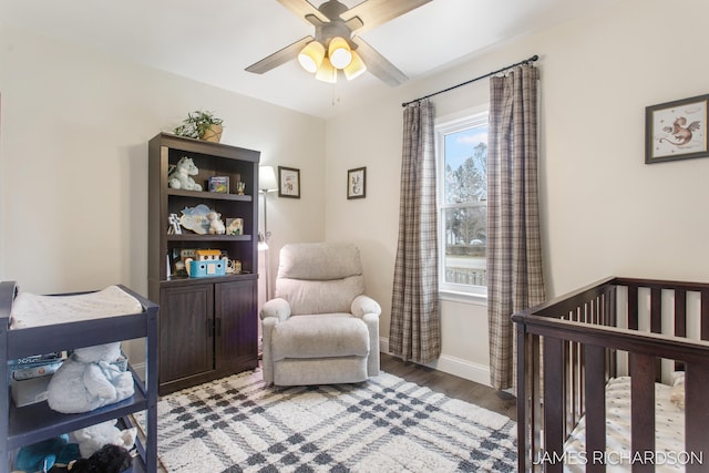 bedroom featuring light wood finished floors, a crib, baseboards, and a ceiling fan