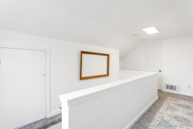 hall with visible vents, baseboards, light colored carpet, lofted ceiling, and an upstairs landing