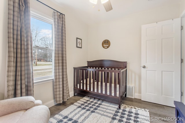 bedroom with wood finished floors, baseboards, multiple windows, and a crib