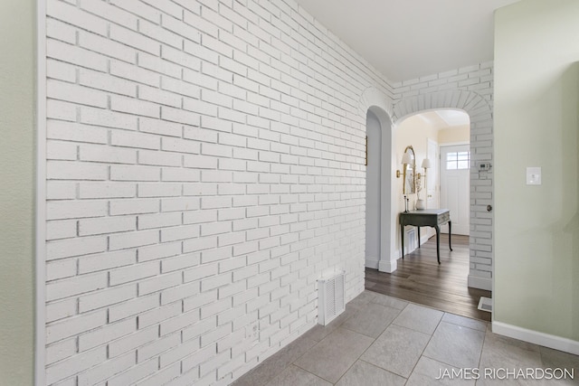 hall featuring visible vents, brick wall, baseboards, arched walkways, and tile patterned floors