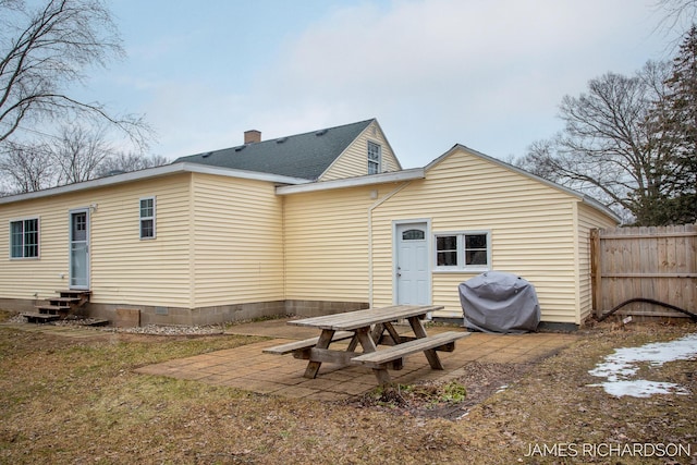 rear view of property featuring entry steps, a patio, fence, a shingled roof, and a chimney