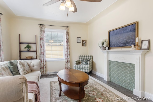 living area with a baseboard heating unit, wood finished floors, baseboards, ceiling fan, and a tile fireplace