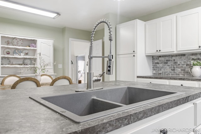 kitchen featuring dark countertops, white cabinets, tasteful backsplash, and a sink