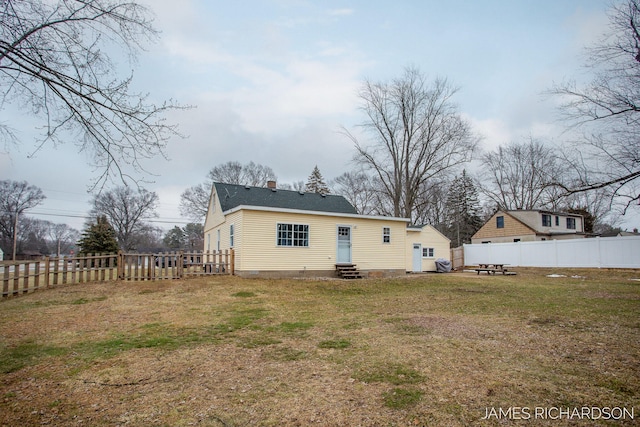 back of house with entry steps, a yard, a fenced backyard, and a chimney