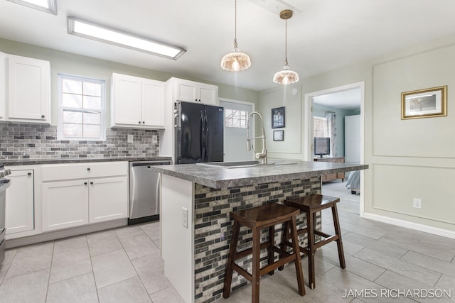 kitchen with a sink, tasteful backsplash, dark countertops, freestanding refrigerator, and dishwasher