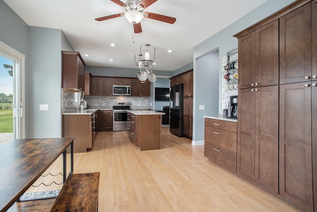 kitchen with a center island, light wood-type flooring, decorative backsplash, appliances with stainless steel finishes, and a ceiling fan