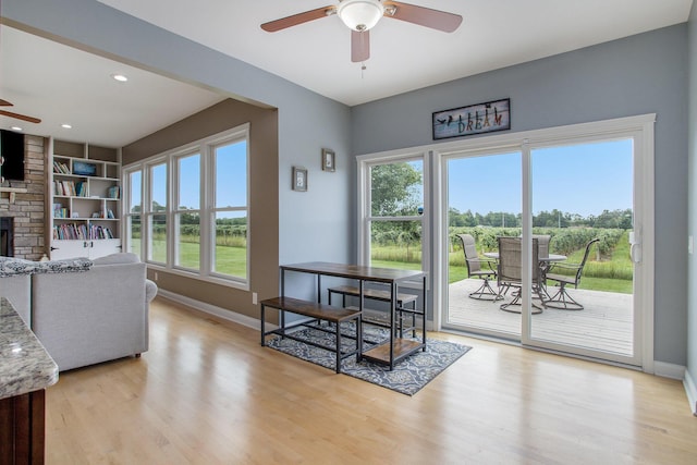 living room with a fireplace, baseboards, light wood-type flooring, and ceiling fan