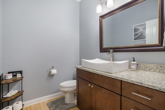 bathroom featuring toilet, vanity, baseboards, and wood finished floors