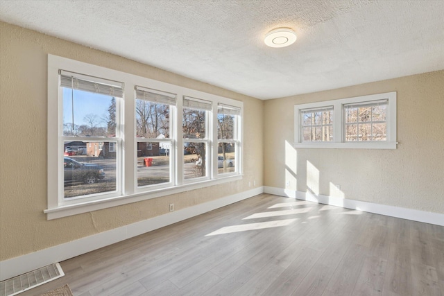 unfurnished room with a wealth of natural light, visible vents, and a textured wall