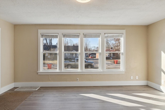 empty room featuring plenty of natural light, wood finished floors, and baseboards