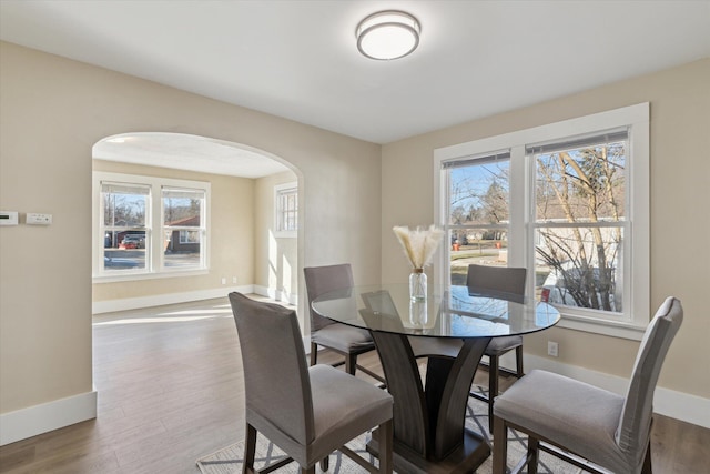 dining room featuring wood finished floors, arched walkways, and a wealth of natural light