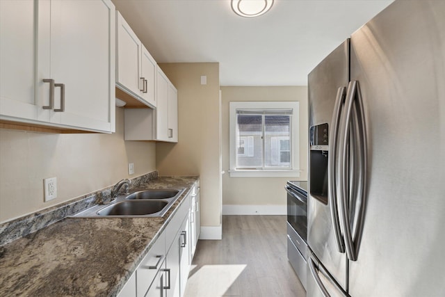 kitchen with baseboards, light wood-style flooring, white cabinets, stainless steel appliances, and a sink