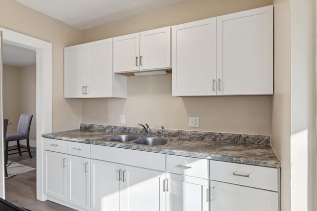 kitchen featuring white cabinets, wood finished floors, baseboards, and a sink