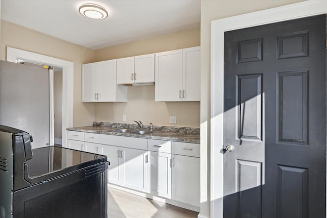 kitchen with black range with electric stovetop, a sink, dark countertops, freestanding refrigerator, and white cabinetry