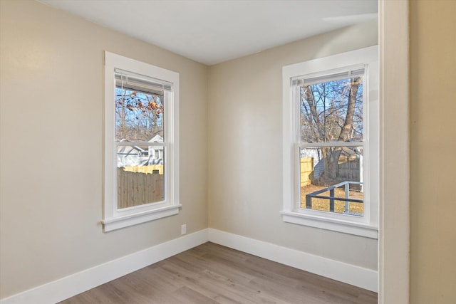 empty room with a healthy amount of sunlight, baseboards, and wood finished floors