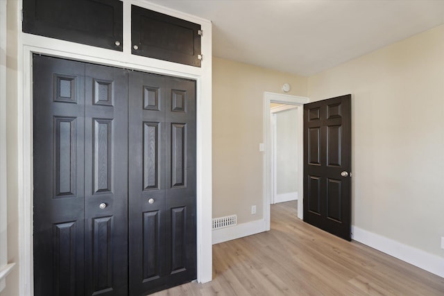 unfurnished bedroom featuring a closet, visible vents, baseboards, and wood finished floors