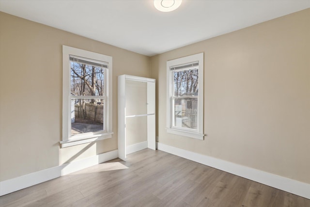 empty room with wood finished floors, a healthy amount of sunlight, and baseboards