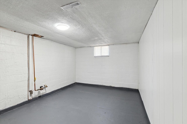 below grade area with visible vents, a textured ceiling, and concrete block wall