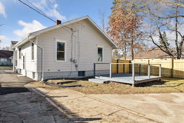 back of house featuring a wooden deck, driveway, a chimney, and fence