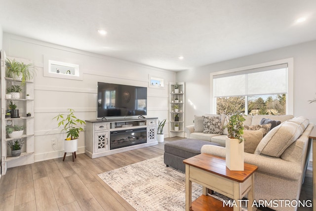 living room featuring light wood finished floors, a glass covered fireplace, recessed lighting, and baseboards