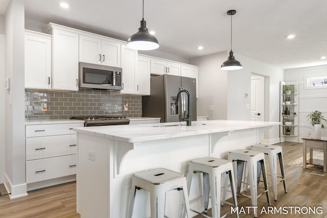 kitchen featuring light wood-style flooring, a kitchen island with sink, stainless steel appliances, decorative backsplash, and white cabinetry