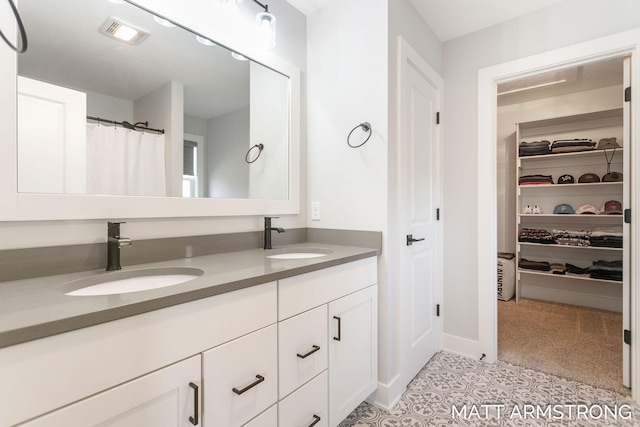 full bath with double vanity, a spacious closet, visible vents, and a sink