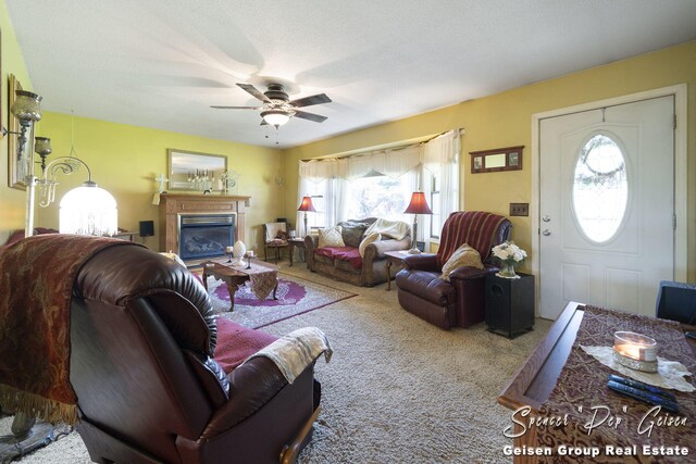 carpeted living room featuring a glass covered fireplace and a ceiling fan