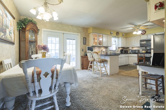 dining room with light carpet, ceiling fan with notable chandelier, french doors, wallpapered walls, and light tile patterned floors