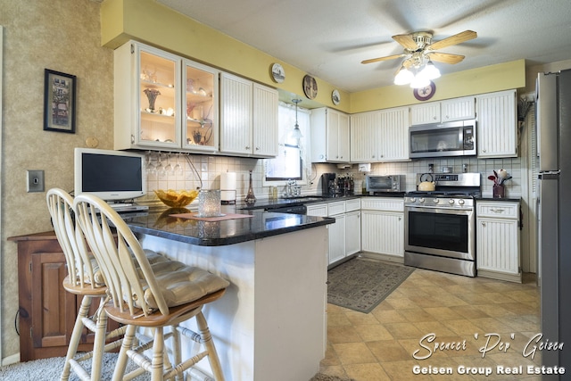 kitchen featuring decorative backsplash, dark countertops, appliances with stainless steel finishes, and a peninsula