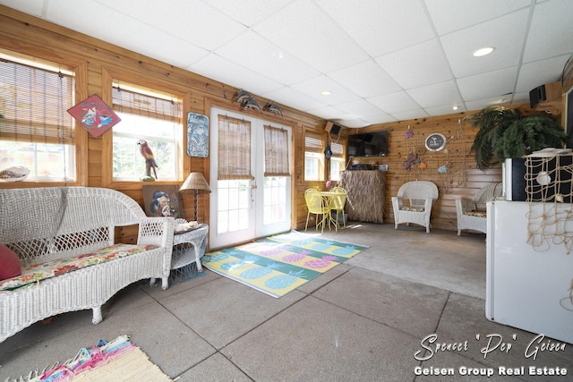 unfurnished living room with a healthy amount of sunlight, wood walls, french doors, and a paneled ceiling