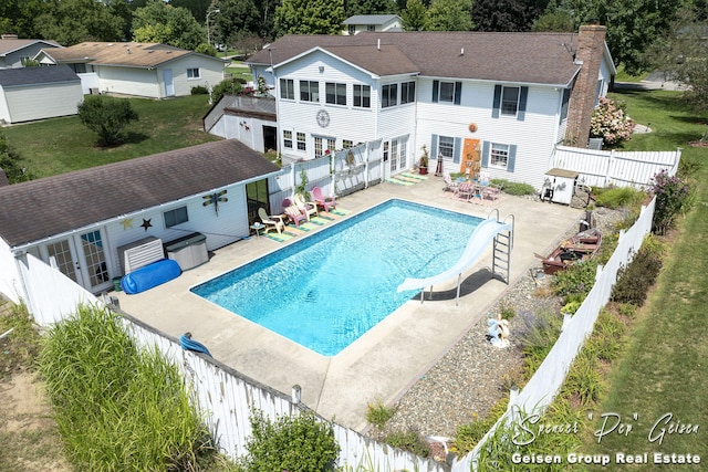 back of house featuring an outbuilding, driveway, a fenced backyard, a fenced in pool, and a chimney