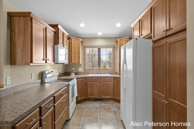 kitchen featuring brown cabinets, a sink, dark countertops, recessed lighting, and white appliances