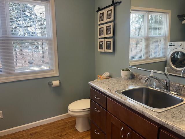 bathroom with baseboards, toilet, vanity, wood finished floors, and washer / clothes dryer